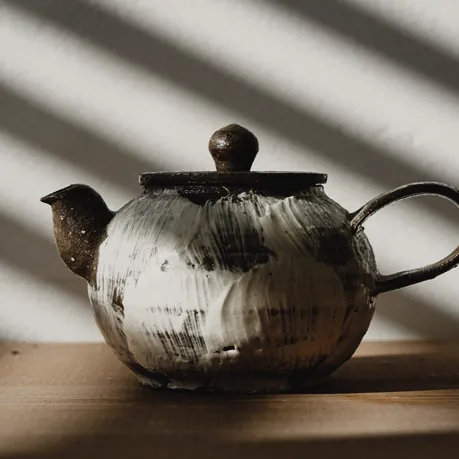 A handmade teapot in striped window light