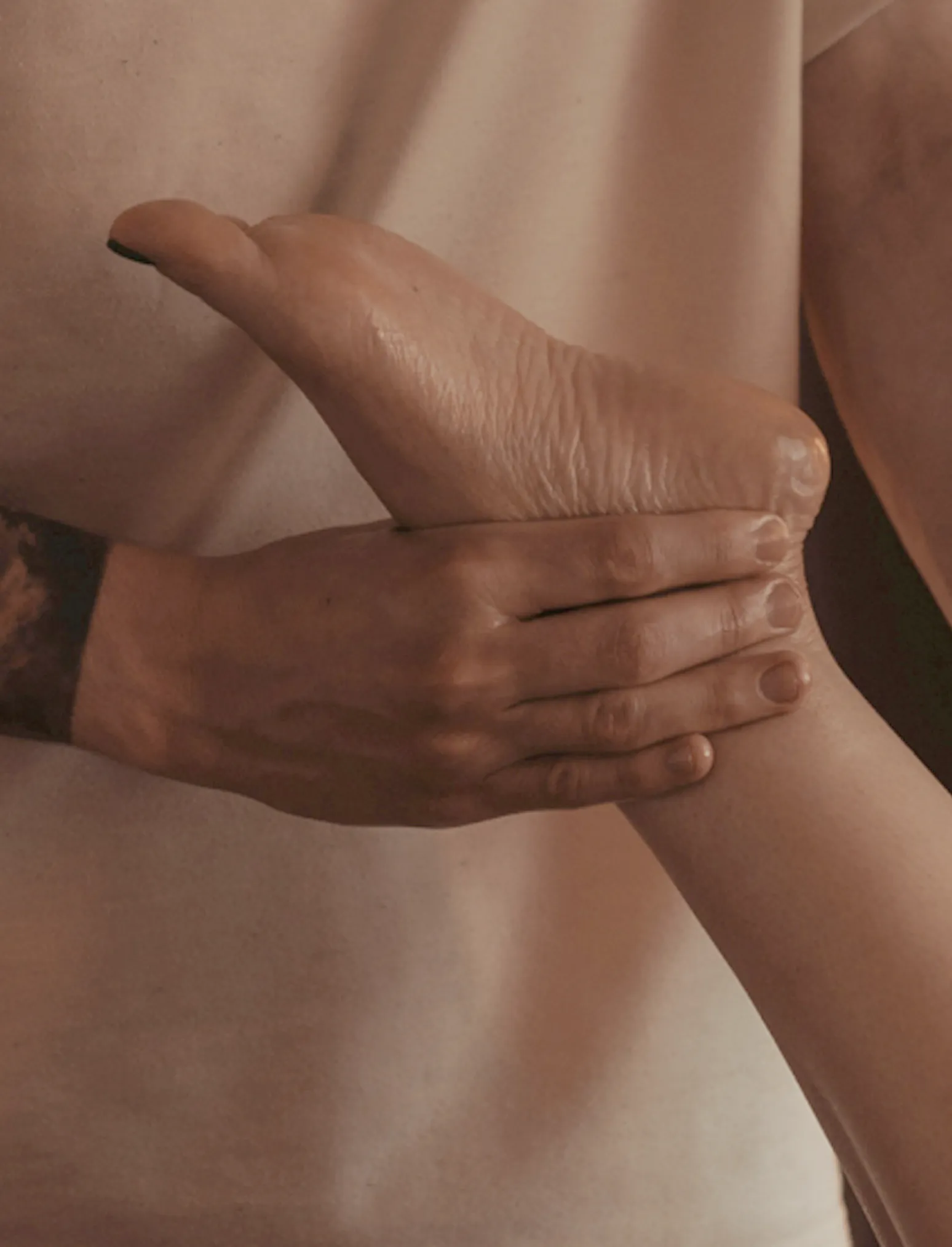 A massage therapist's hand holding the client's foot, lamp light on the skin