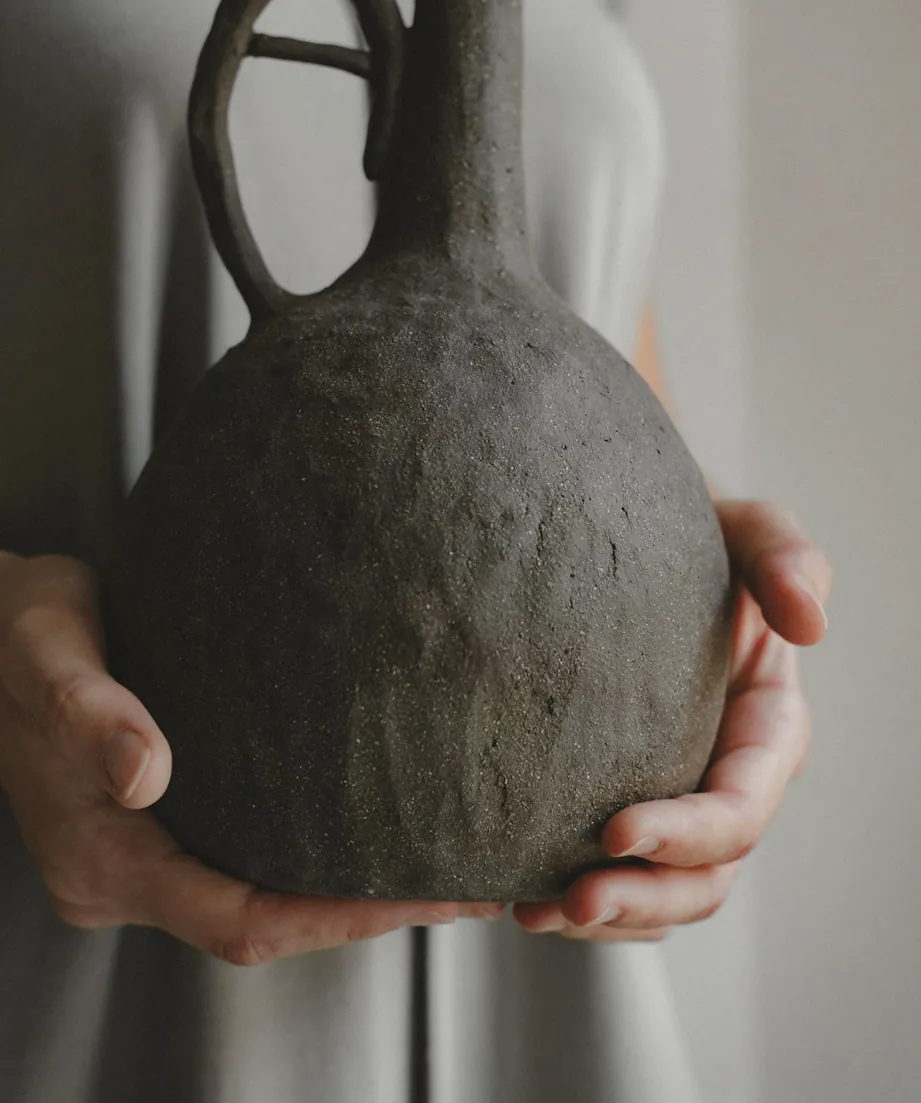 Two hands holding a dark handmade clay jug