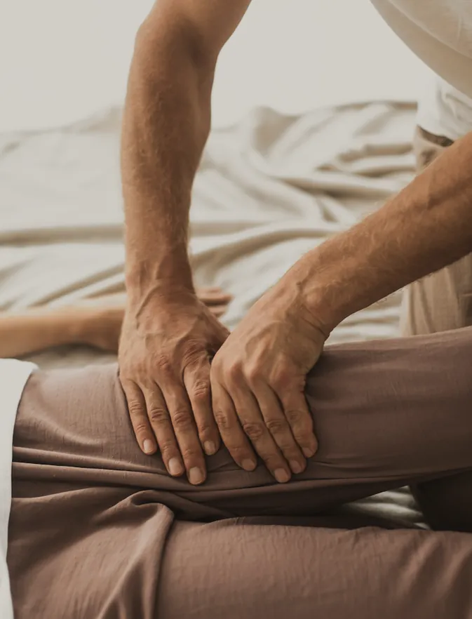 Both hands working slowly along the thigh of someone lying on a soft mattress