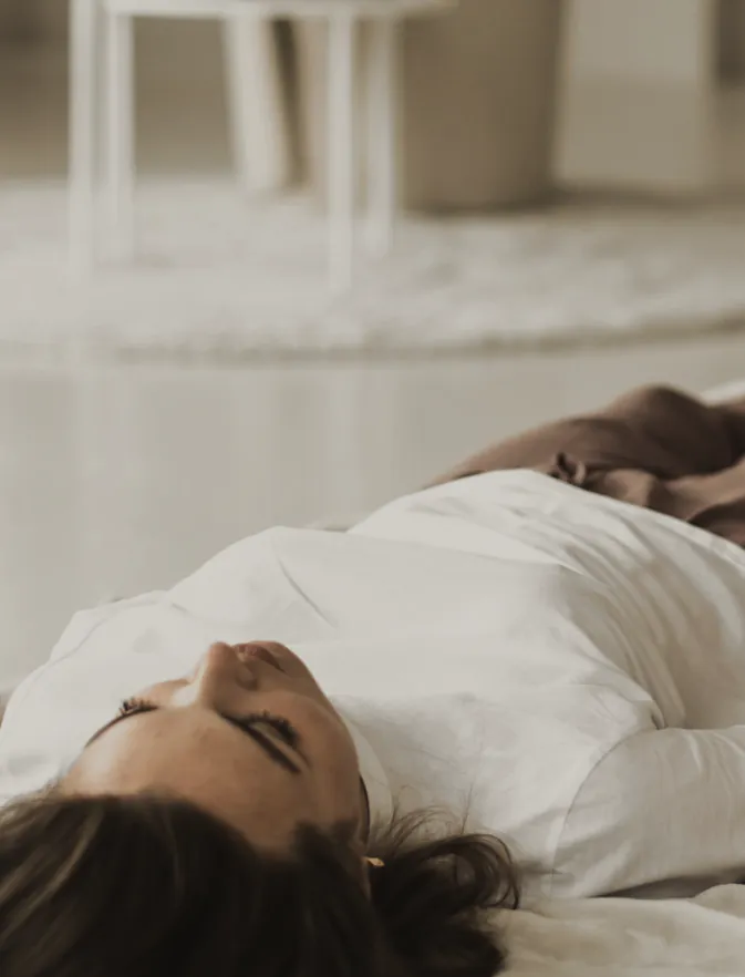 A woman lying still with her eyes closed in a pale room