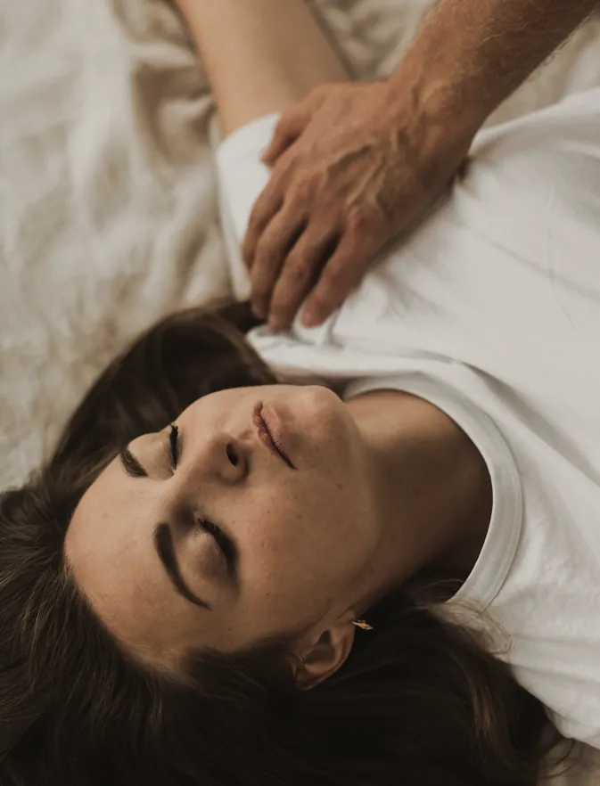 A woman lying back with her eyes closed, a hand resting on her shoulder