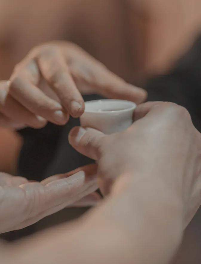 Two people's hands meeting round a small white cup of tea
