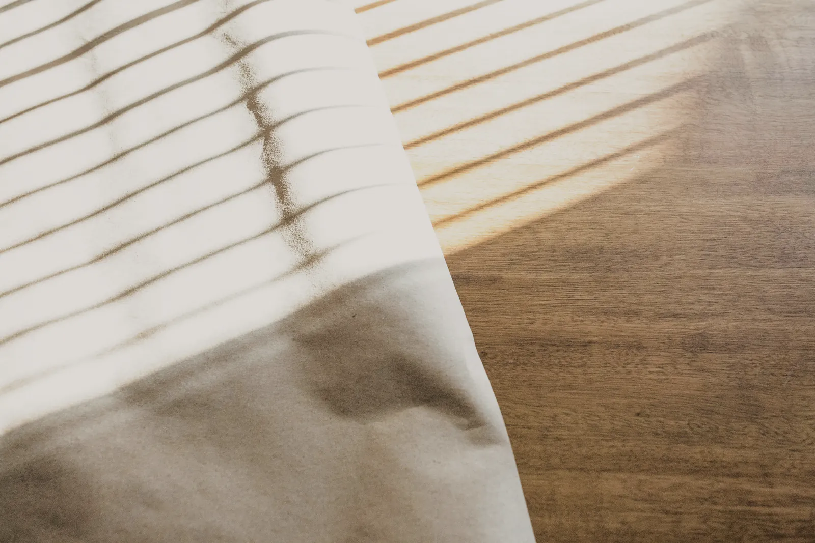 Low sun falling in stripes across a white sheet on a timber table