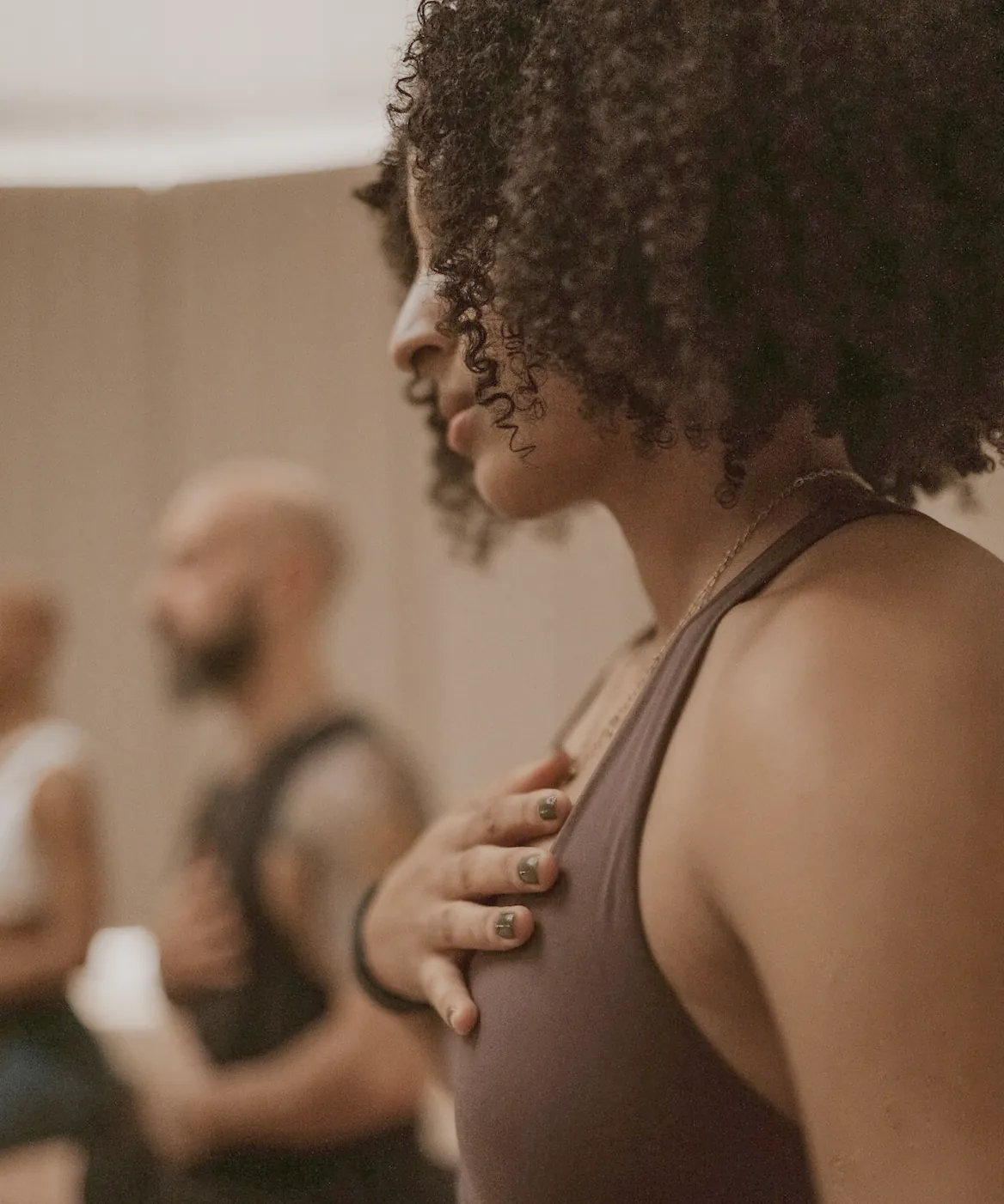 A woman with one hand on her chest, breathing slowly, the small class behind her