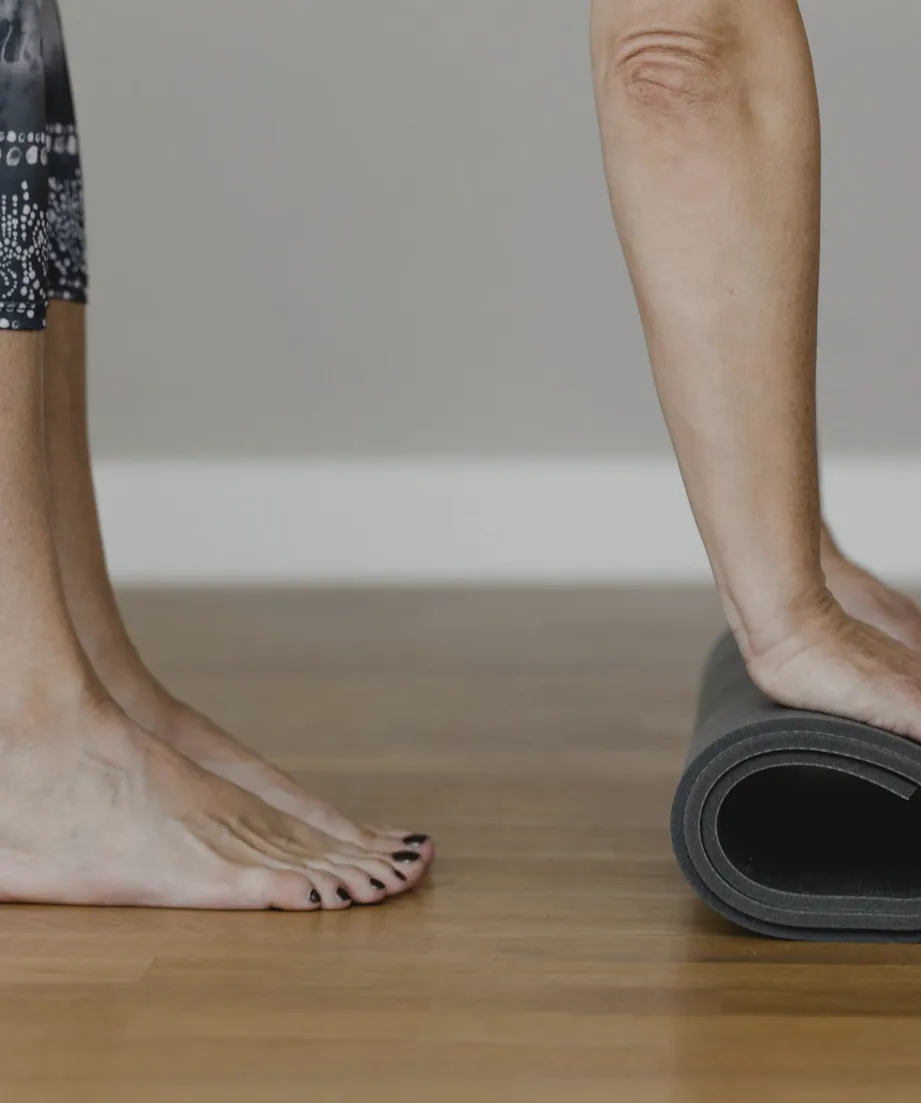 Bare feet on a timber floor as someone rolls up a grey mat