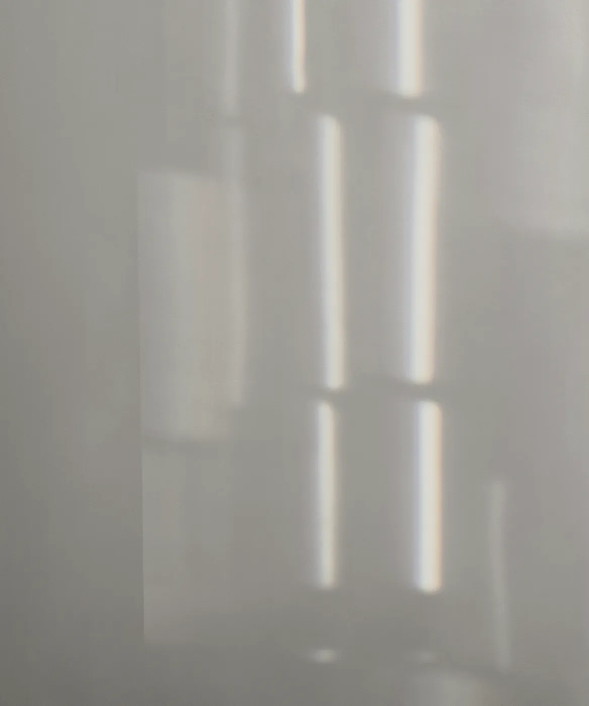 Window light falling on a pale wall in soft bars, a faint rainbow at each edge