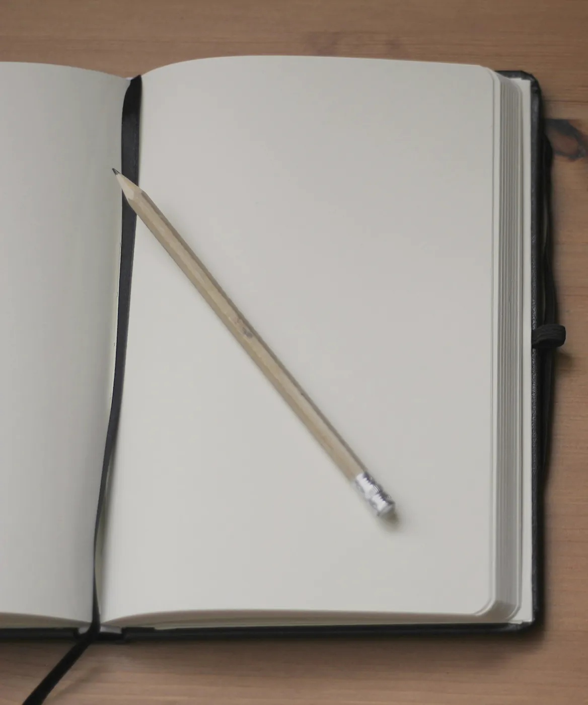 An open notebook with blank pages and a pencil on a timber desk