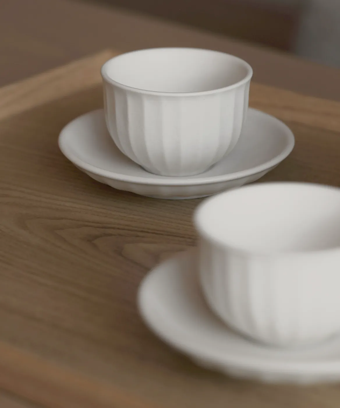 Small white cups and dishes on a timber table in soft window light