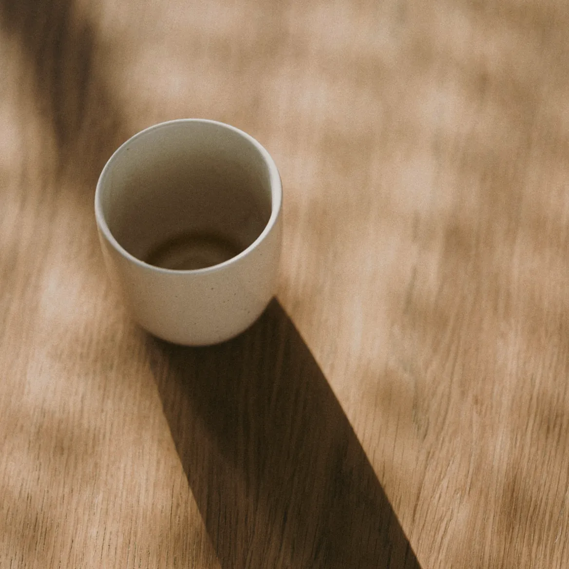 An empty cup and its long shadow on warm timber