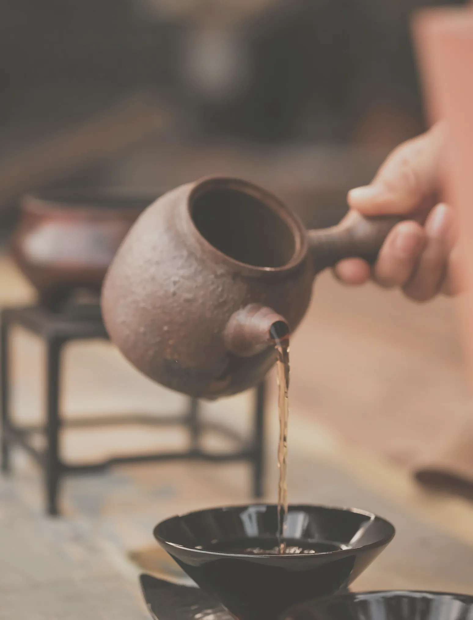 Tea poured from a clay pot into a dark bowl