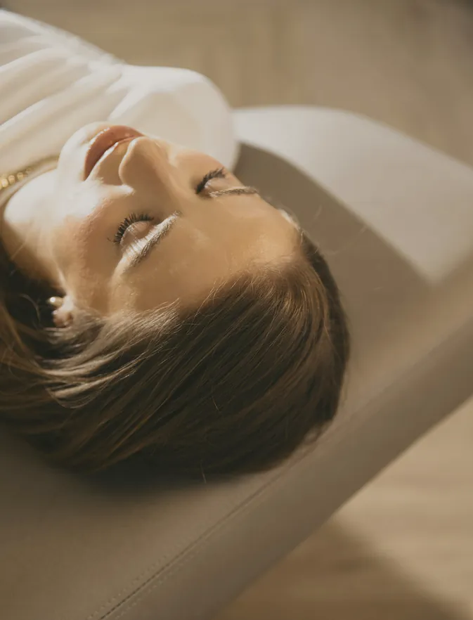 A woman resting on a treatment table with her eyes closed