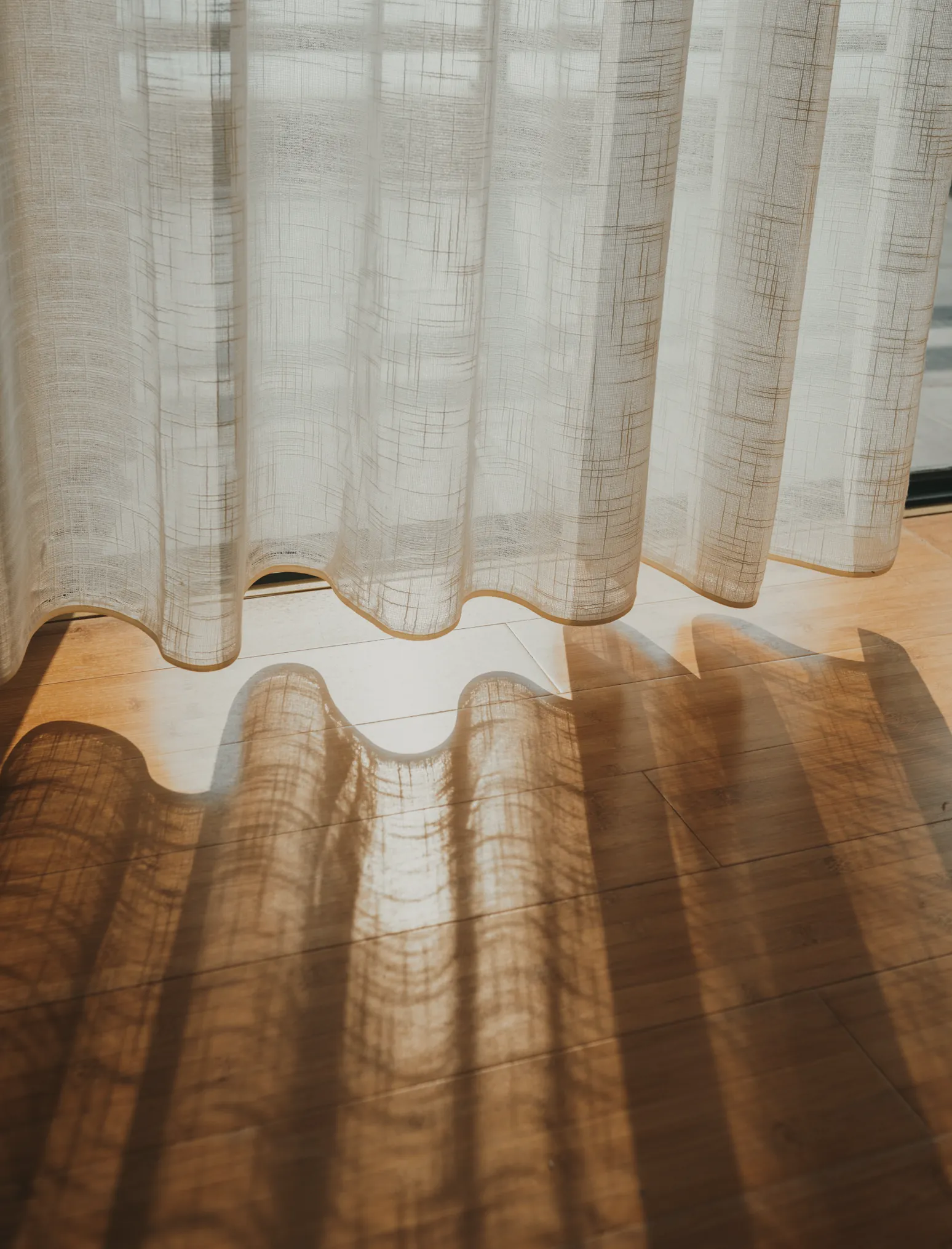 A sheer linen curtain glowing above a timber floor