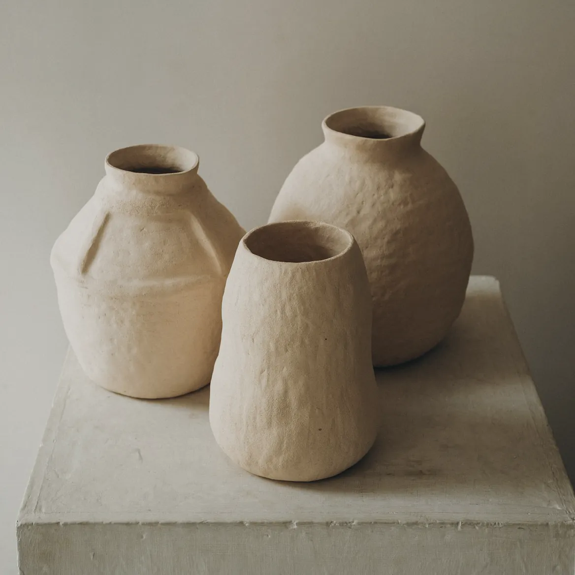 Three handmade clay jars on a plaster plinth