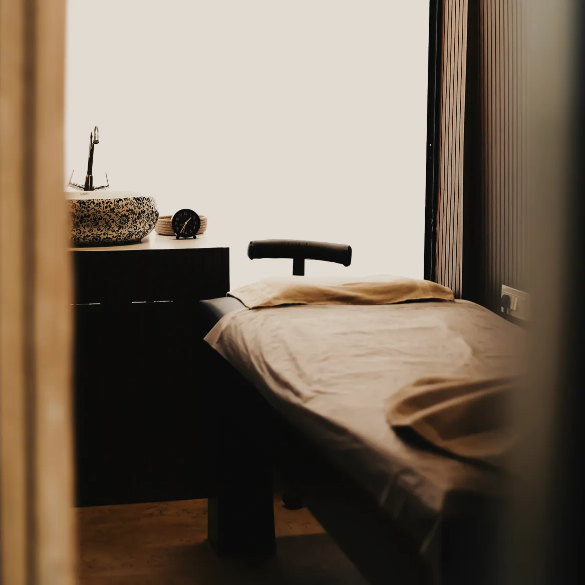 A made treatment table beside a tall window in a timber lined room