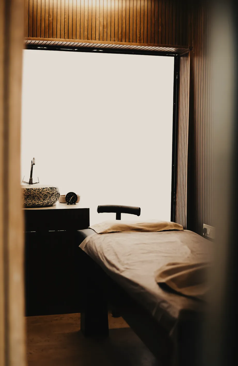 A made treatment table beside a tall window in a timber lined room