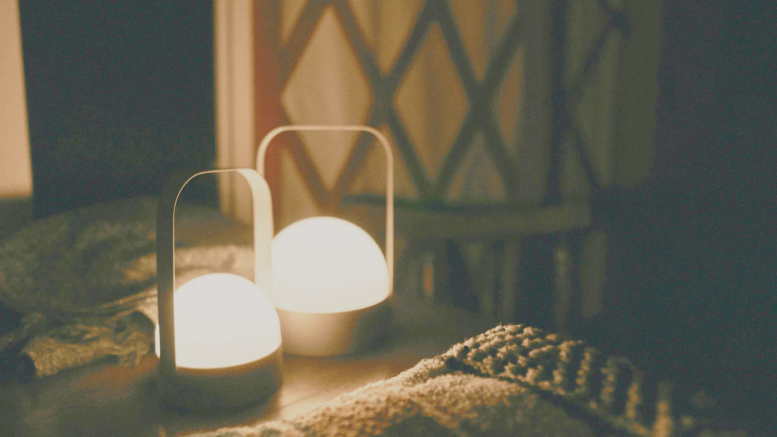 Two small lamps glowing on a heavy knitted blanket in a dark room
