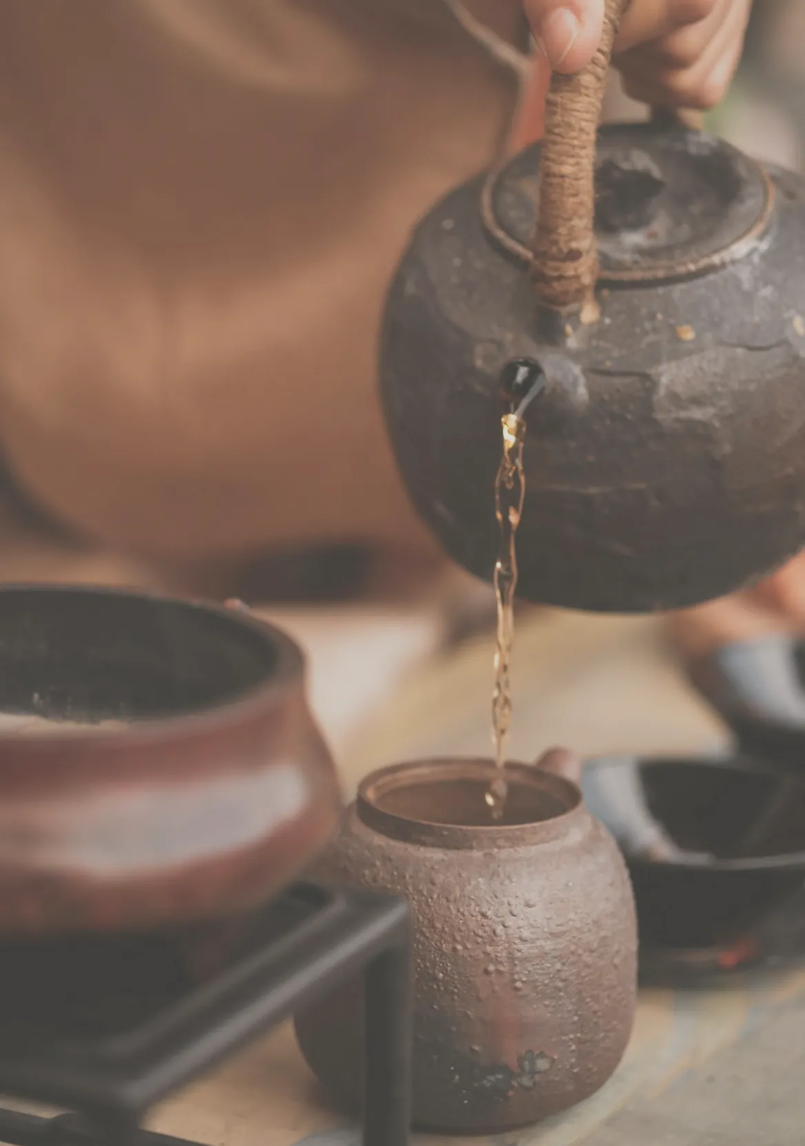 Tea poured from a dark iron pot into a small clay cup