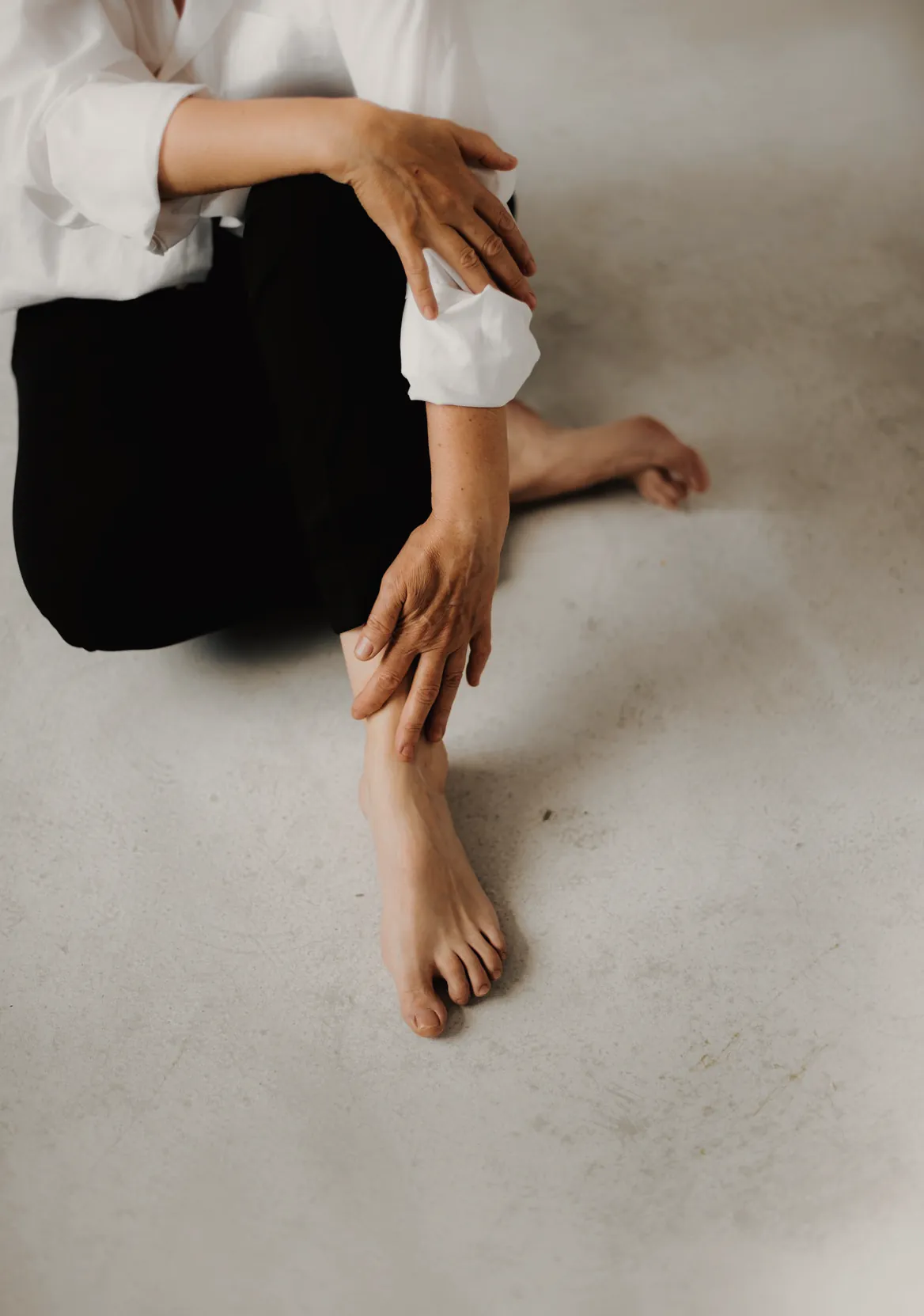 Someone sitting barefoot on the floor in a loose shirt and soft trousers